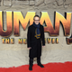 Jake Kasdan, in a black coat and navy scarf, stands in front of a Jumanji: The Next Level backdrop.